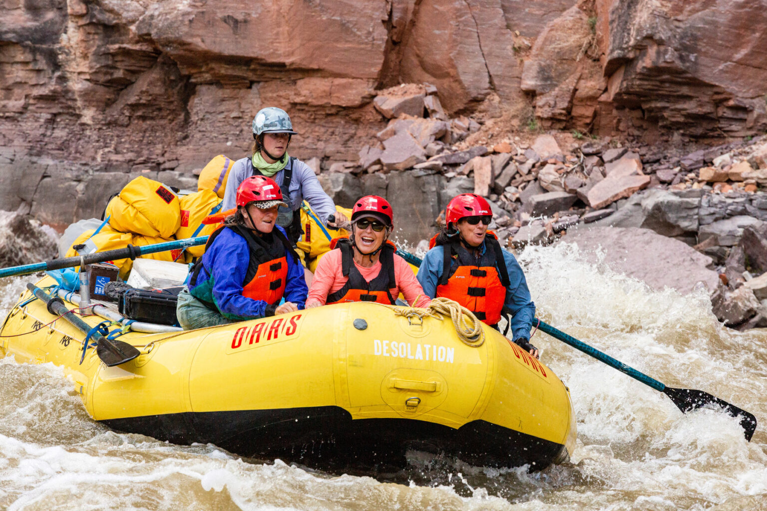 Three women in the front of an oar raft while a guide rows them through rapids on the Yampa River in Utah