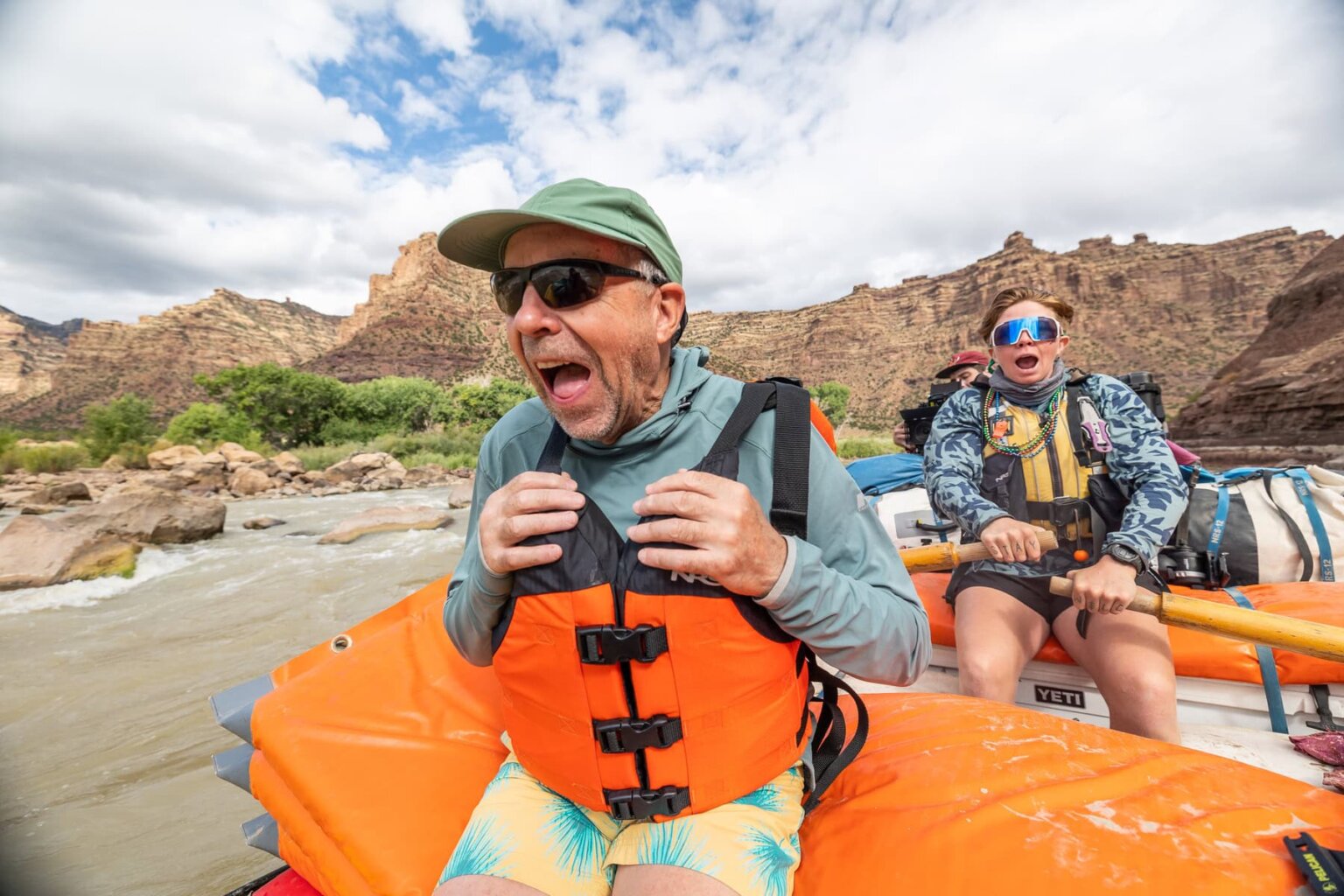 A man sits in the front of a raft with a big grin on his face as his expressive guide rows
