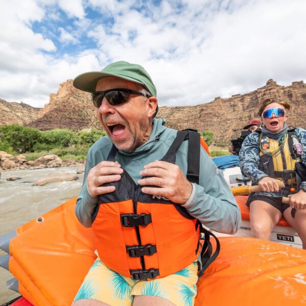 A man sits in the front of a raft with a big grin on his face as his expressive guide rows