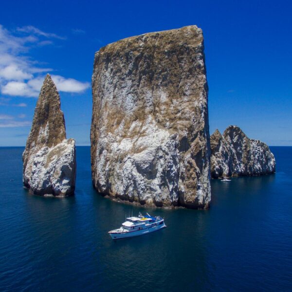 A luxury yacht in front of massive rocks coming out of the ocean in the Galapagos.