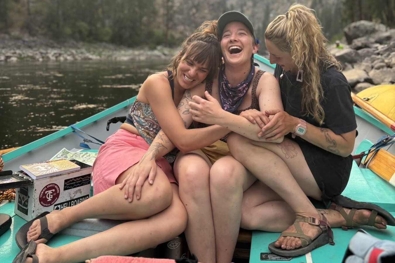 Three women laugh and hug on a dory on the Main Salmon River in Idaho