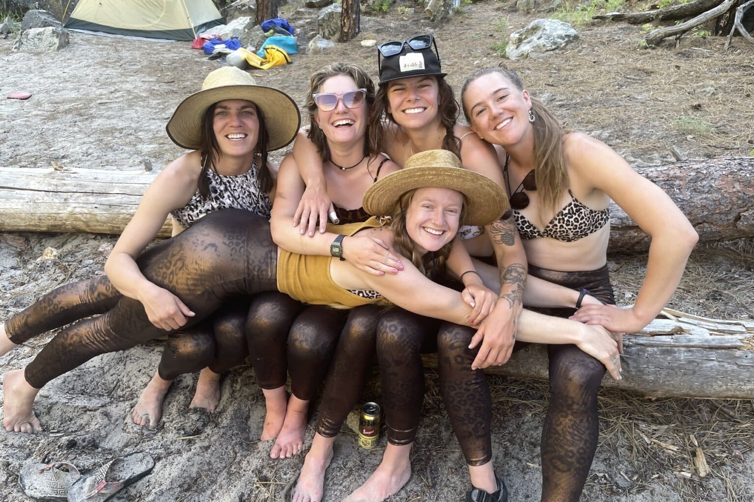 A woman lays across the laps of four other women as they smile for the camera wearing leopard print tops and matching leggings.