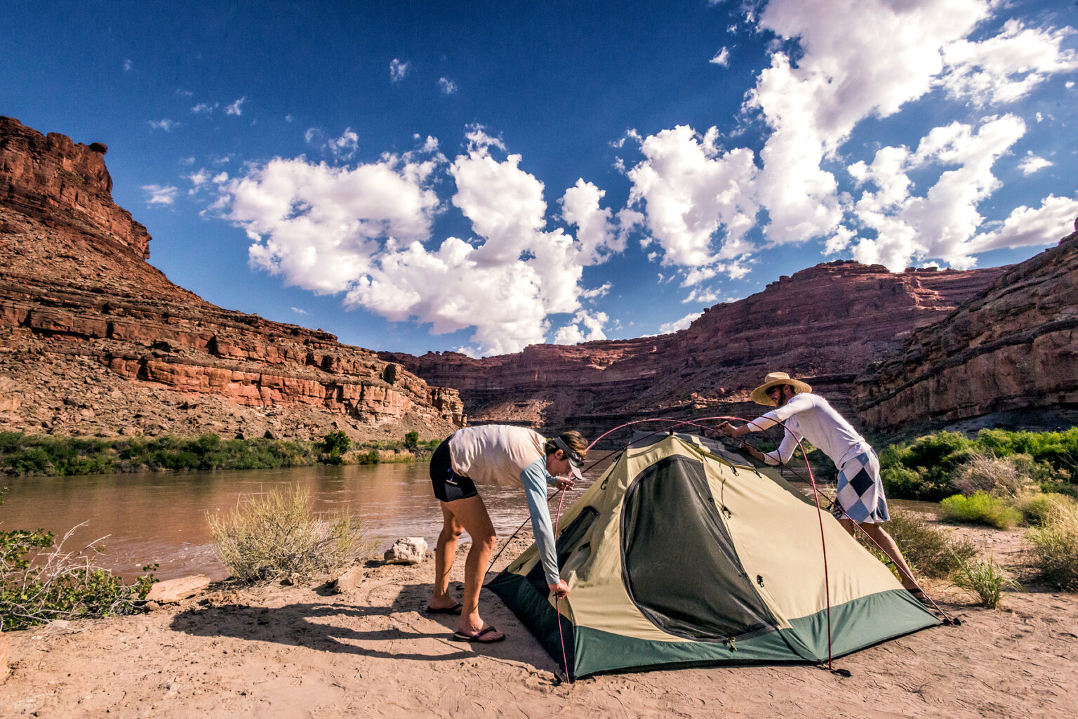 Two campers setting up a tent on the shore of the Colorado River on a Cataract Canyon rafting trip.