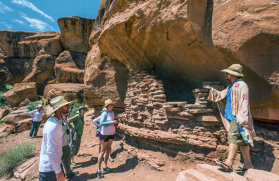A guide draped in a sarong gives an interpretive talk while serveral guests listen at an archeological site in Canyonlands National Park.