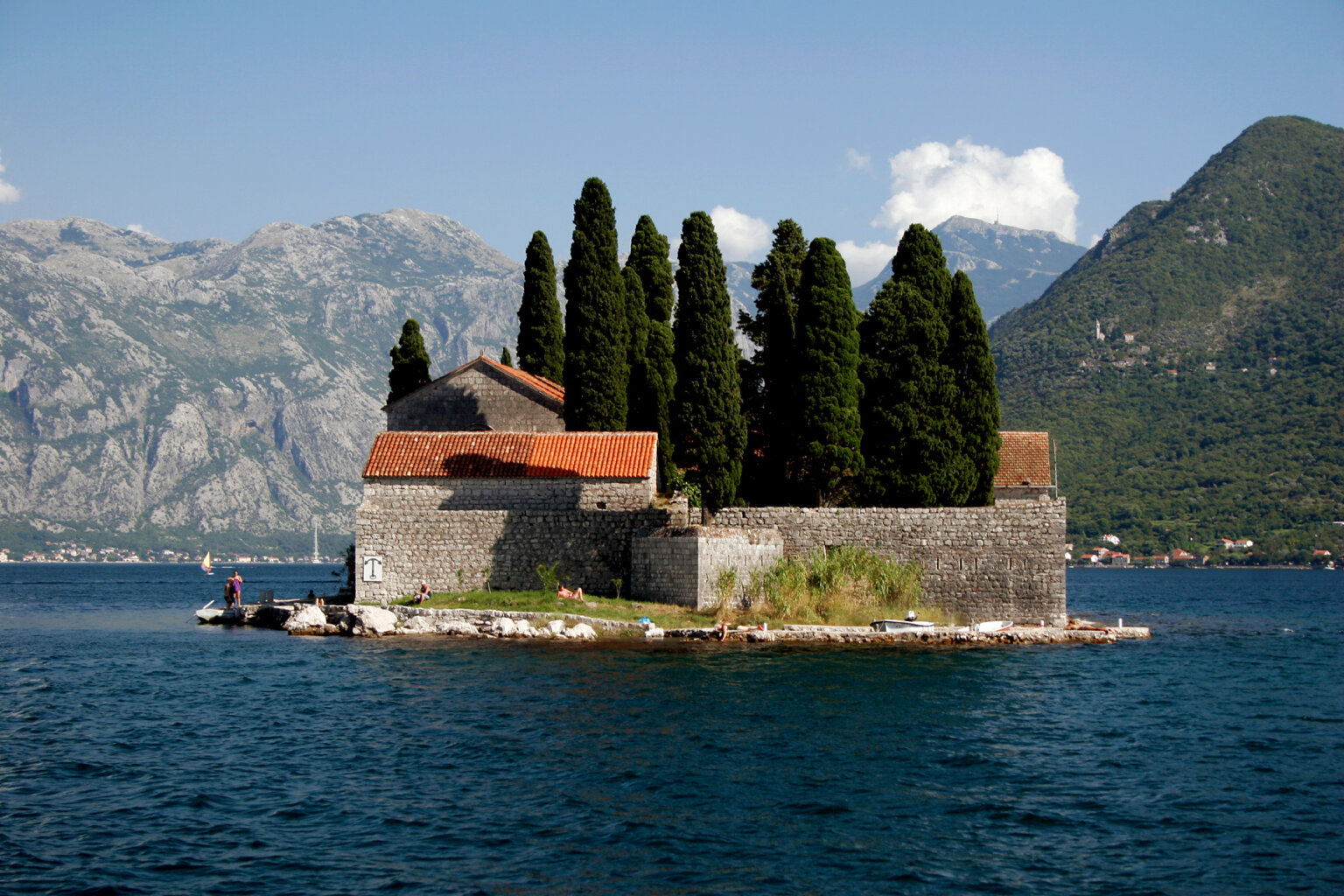 A historical building on a small island in Croatia with large green trees rising out of the courtyard.