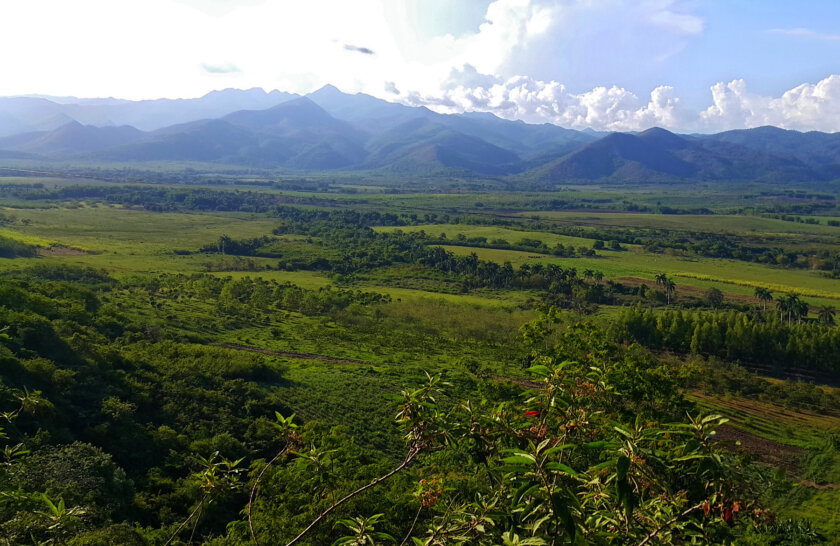 Wide view of the vibrant green landscape of Cuba with verdant mountains rising in the background.