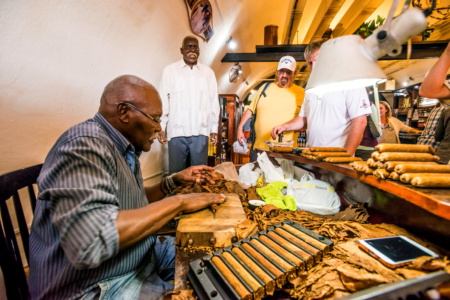 A man hand rolls cigars in a cigar shop in Cuba as a group of tourists watch.
