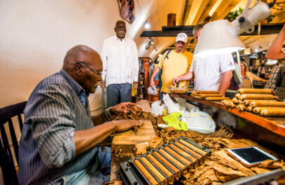 A man hand rolls cigars in a cigar shop in Cuba as a group of tourists watch.