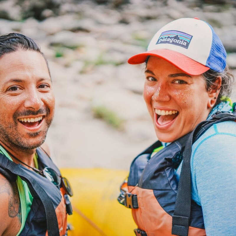 Two members of the LGBTQ+ community smile at the camera from the front of a yellow raft on the Main Salmon River in Idaho