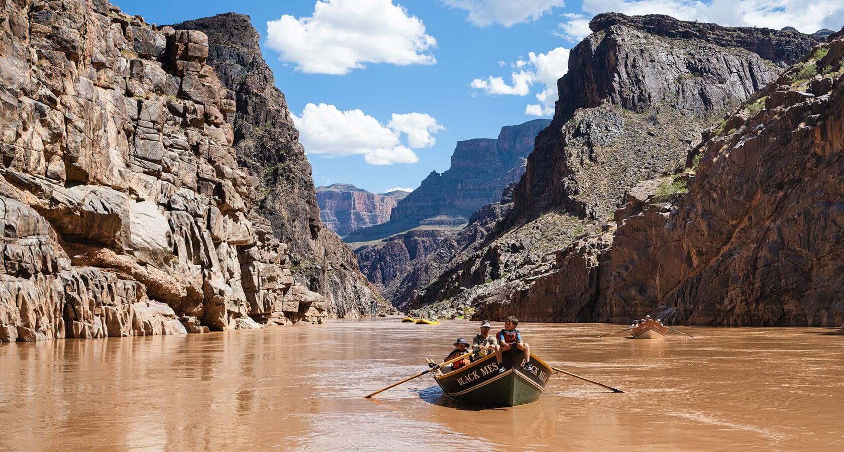 A group in a dory boat glides down the river, framed by the breathtaking canyon walls of the Grand Canyon.