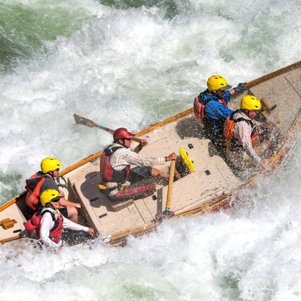 A dory rowed by a guide with four guests crashes through a frothy rapid on the Colorado River in Grand Canyon