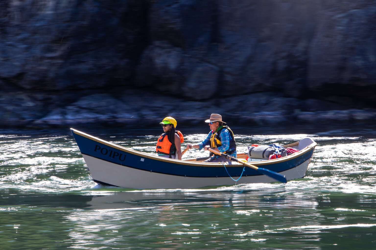 A guest rides in the front of a dory while a guide rows down a flat section of water on the Snake River.