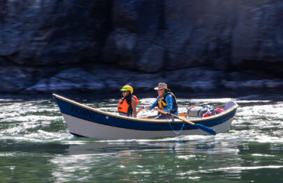 A guest rides in the front of a dory while a guide rows down a flat section of water on the Snake River.
