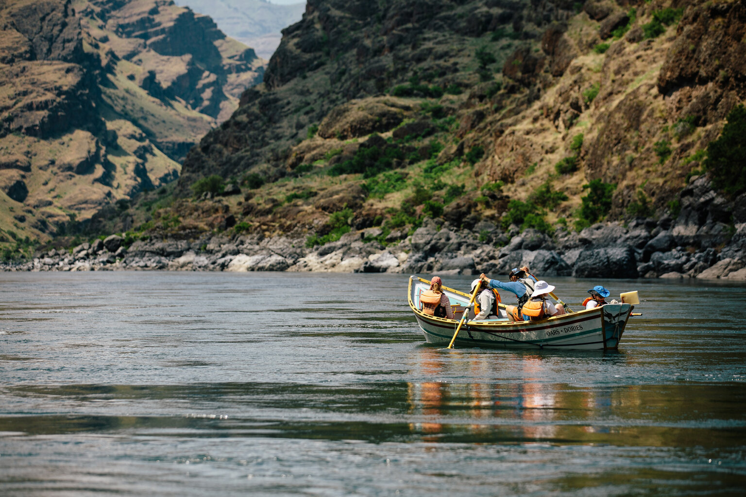 Four guests sit in a dory as a guide rows them down a calm section of the Snake River.
