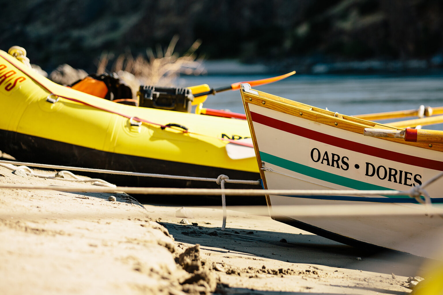 A ground level view close up of a dory and yellow raft tied up on a sandy shore along the river.