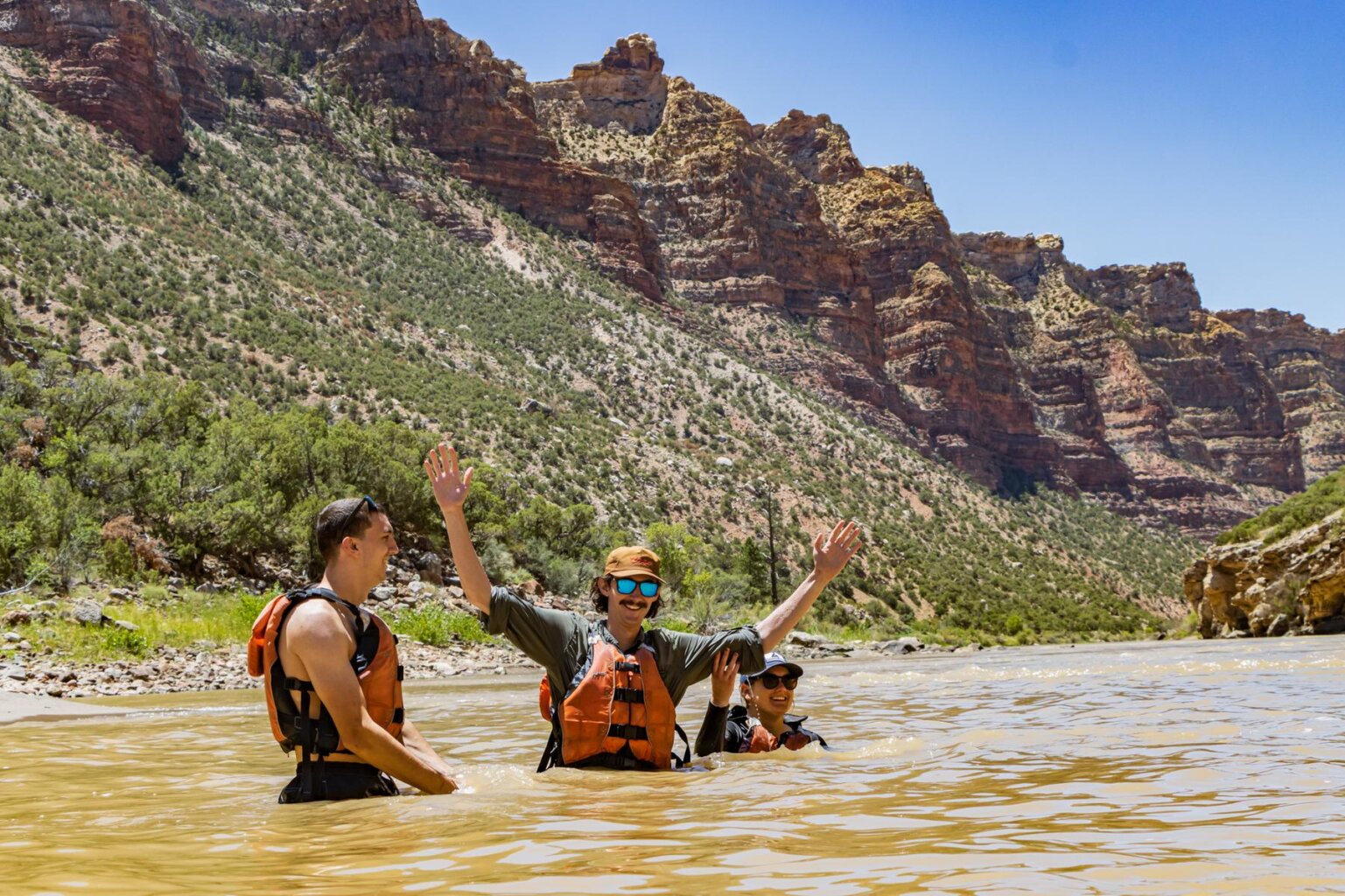 Three adult guests in personal flotation devices have a swim in the Green River through Split Mountain.