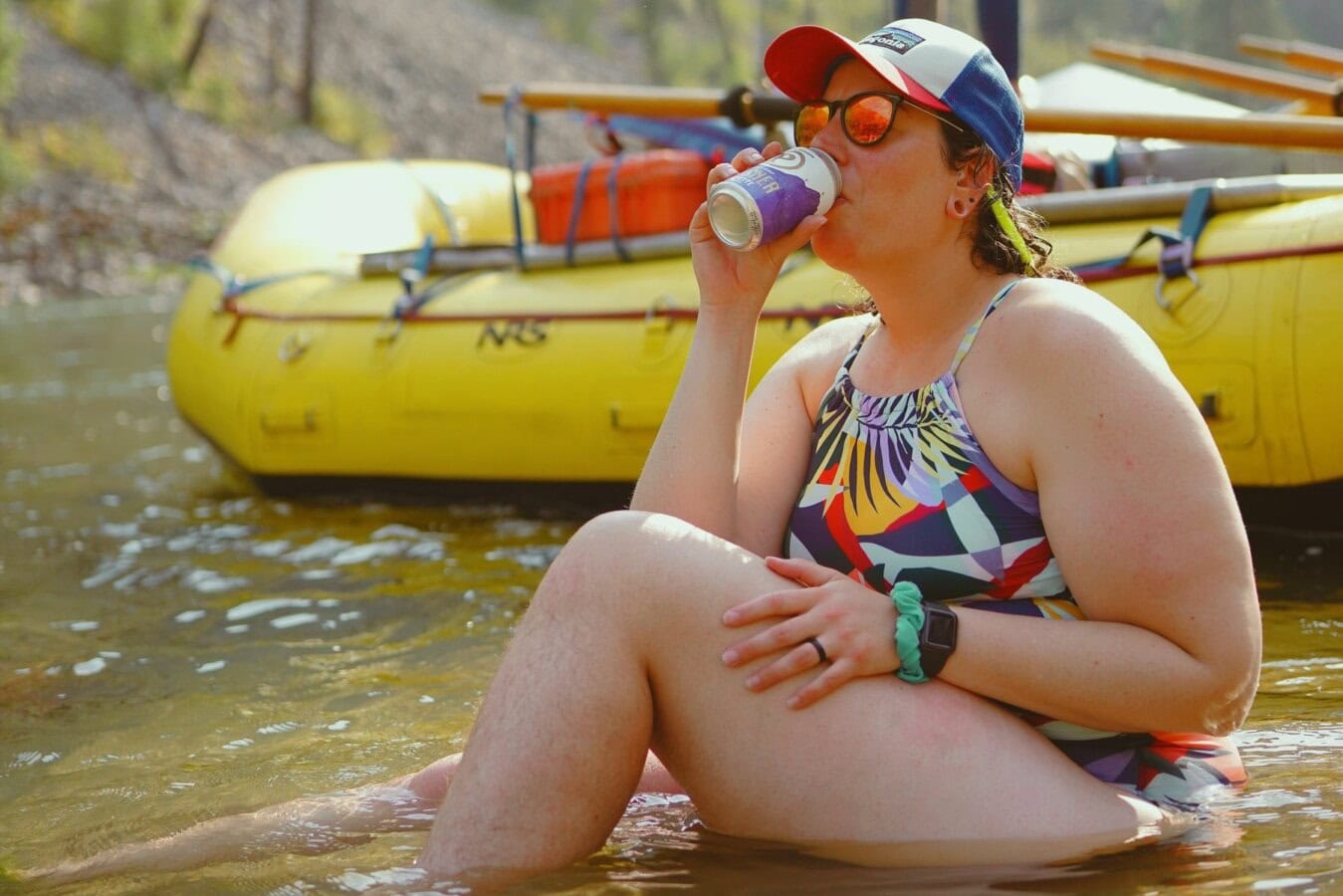 A woman sits in a shallow section of the Main Salmon River and sips on a beverage.