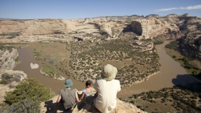 Three people sit on a scenic overlook and the geologic layers of the Yampa River in Dinosaur National Monument
