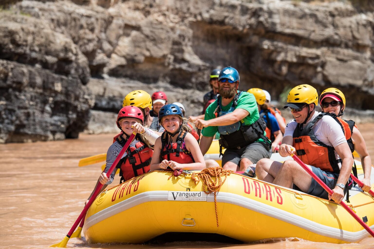 A yellow raft full of guests smile as they paddle down the Green River through the Gates of Lodore.