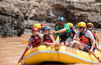 A yellow raft full of guests smile as they paddle down the Green River through the Gates of Lodore.