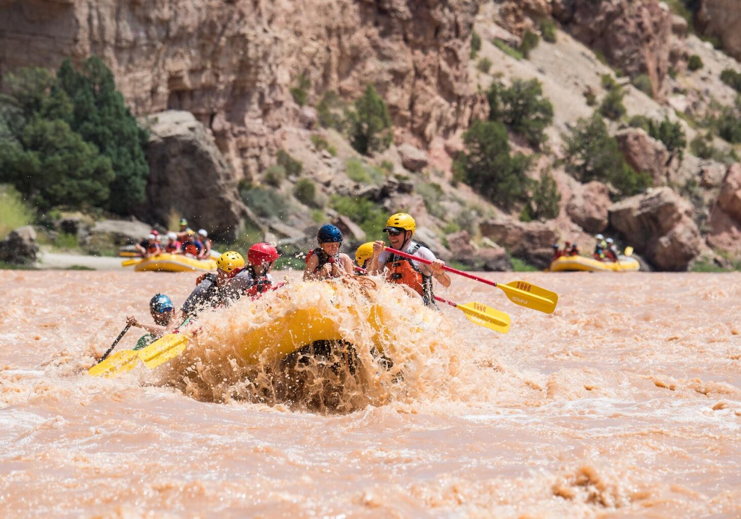 A yellow paddle raft full of guests crash through a rapid on the Green River.