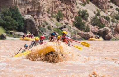 A yellow paddle raft full of guests crash through a rapid on the Green River.
