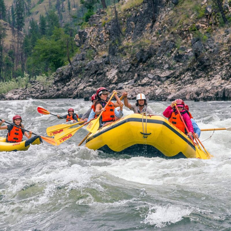 A paddle boat full of people and two solo kayakers take on a rapid on the Main Salmon River in Idaho.
