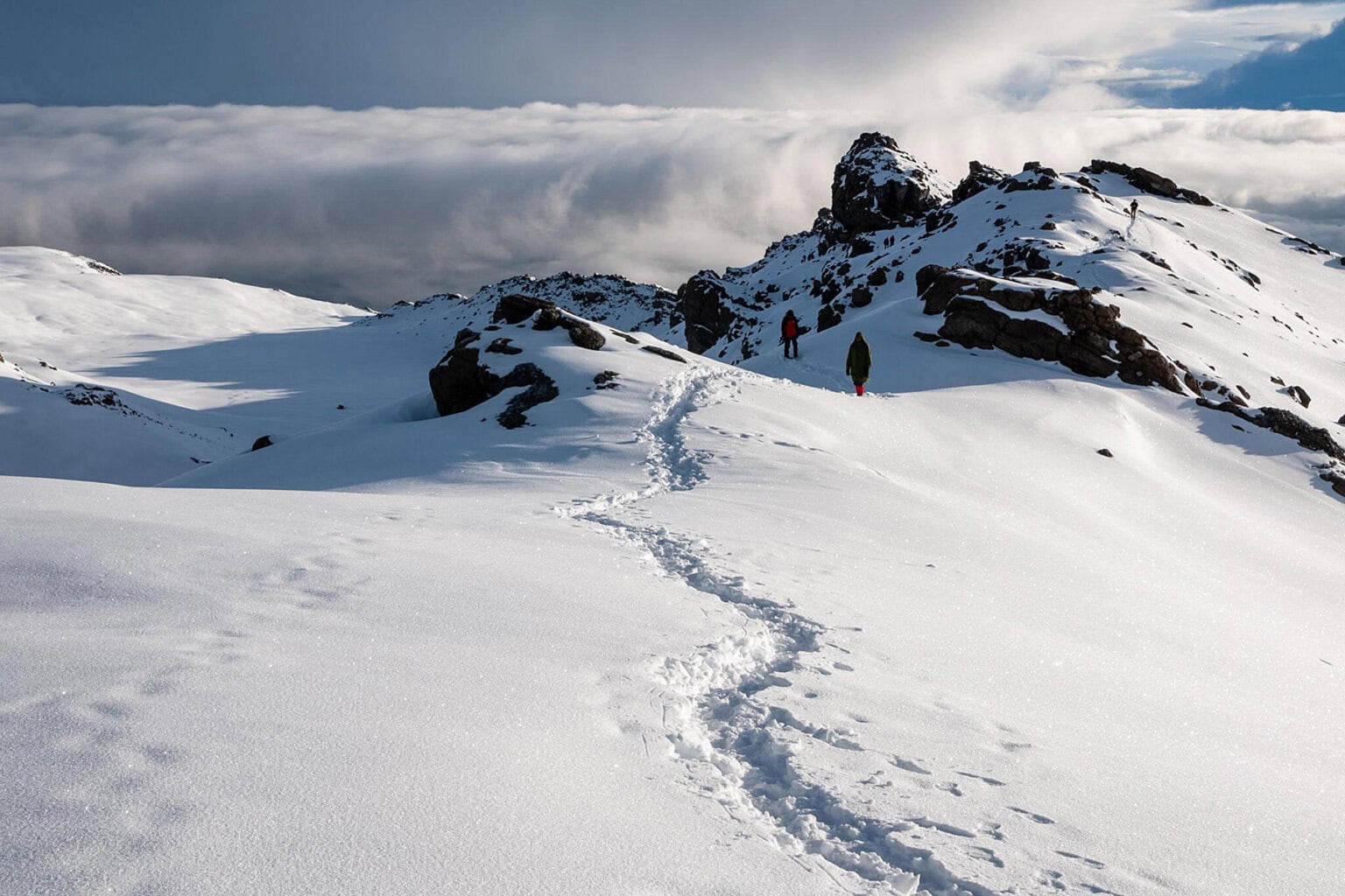 Hikers traverse a snow-covered trail that leads to the summit of Mount Kilimanjaro