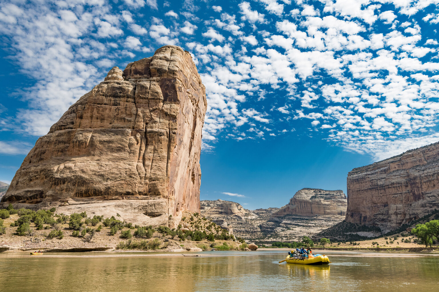 A yellow raft on the river with the impressive and massive Steamboat Rock in the background.