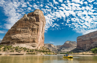 A yellow raft on the river with the impressive and massive Steamboat Rock in the background.