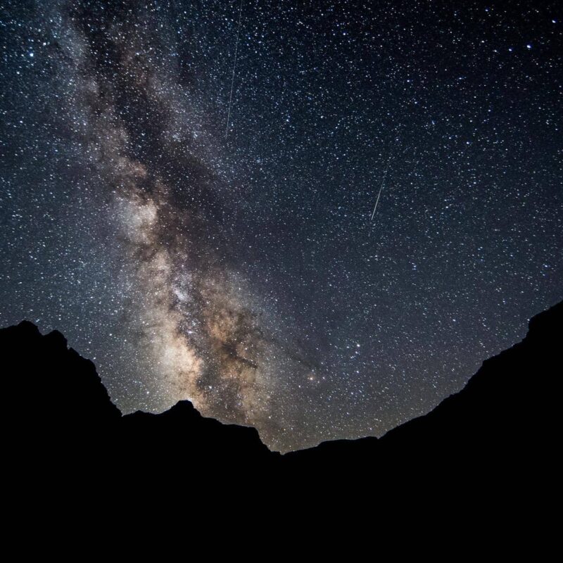A vibrant Milky Way and starry sky above the outline of black canyon walls on an OARS river trip.