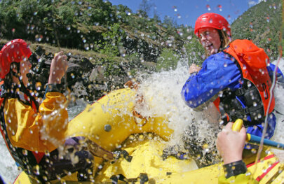 Close up view from behind of two excited guests in the front of a raft as a wave crashes over the boat splashing them.