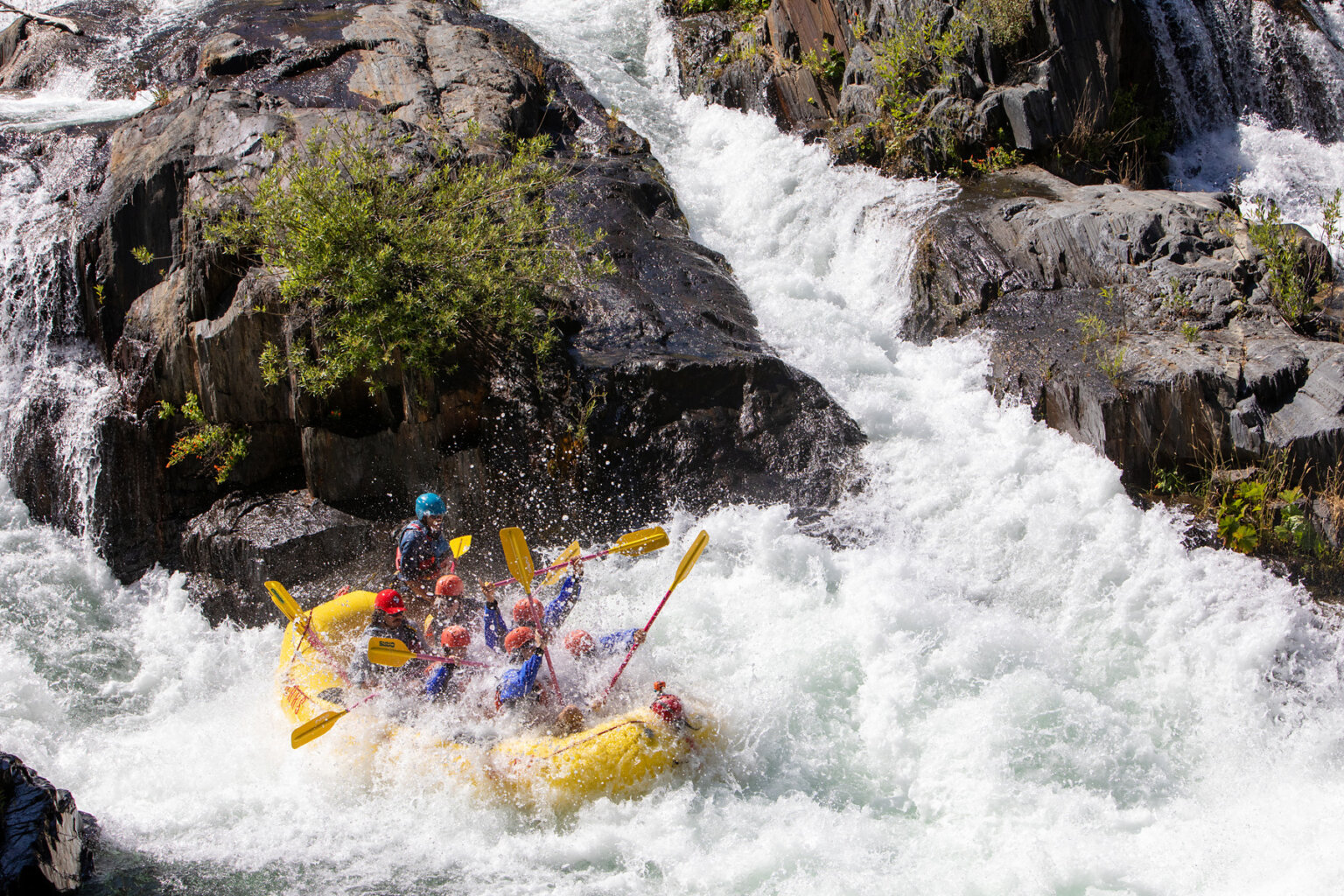 A group of paddlers in a yellow raft are submerged by the huge spray of a wave in a monstrous rapid.