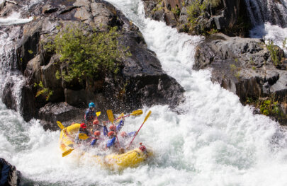 A group of paddlers in a yellow raft are submerged by the huge spray of a wave in a monstrous rapid.