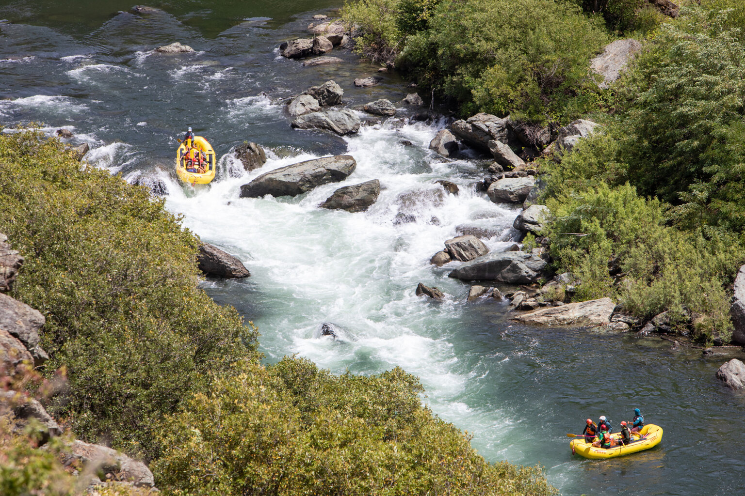 View from above of a yellow raft dropping into a big rapid while another raft downstream watches.