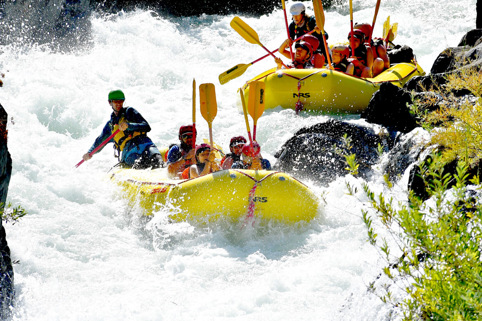 Two yellow rafts full of hunkered down paddlers as they go through a massive rapid on the Middle Fork American River steared through by their guides.