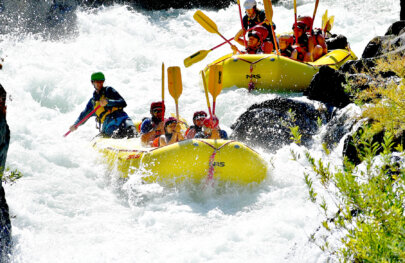 Two yellow rafts full of hunkered down paddlers as they go through a massive rapid on the Middle Fork American River steared through by their guides.