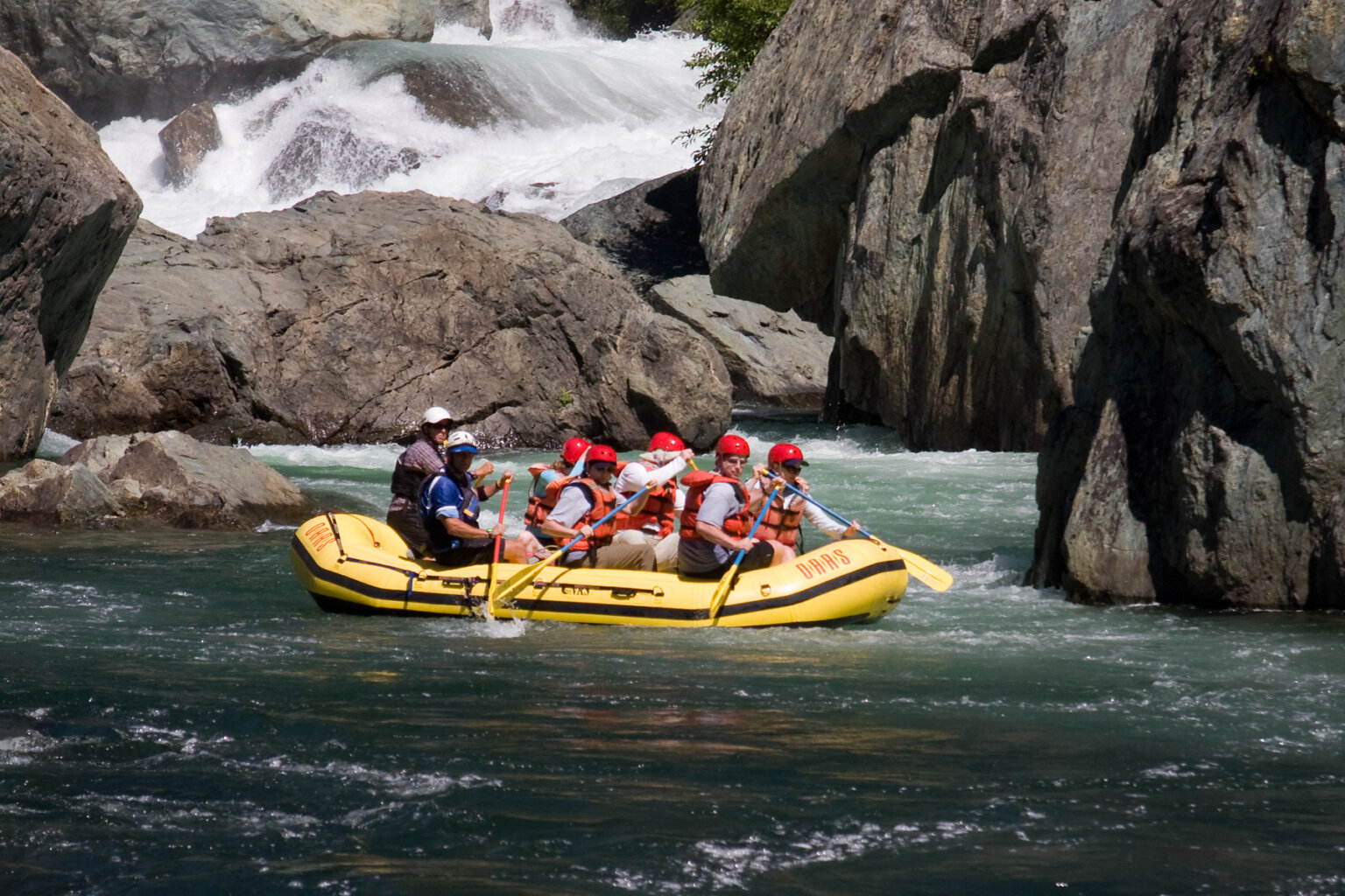 Side view of a yellow raft full of paddlers on the Middle Fork American River surrounded by massive boulders.