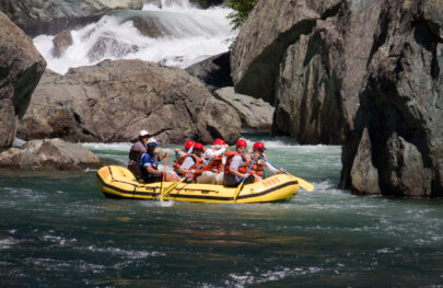 Side view of a yellow raft full of paddlers on the Middle Fork American River surrounded by massive boulders.