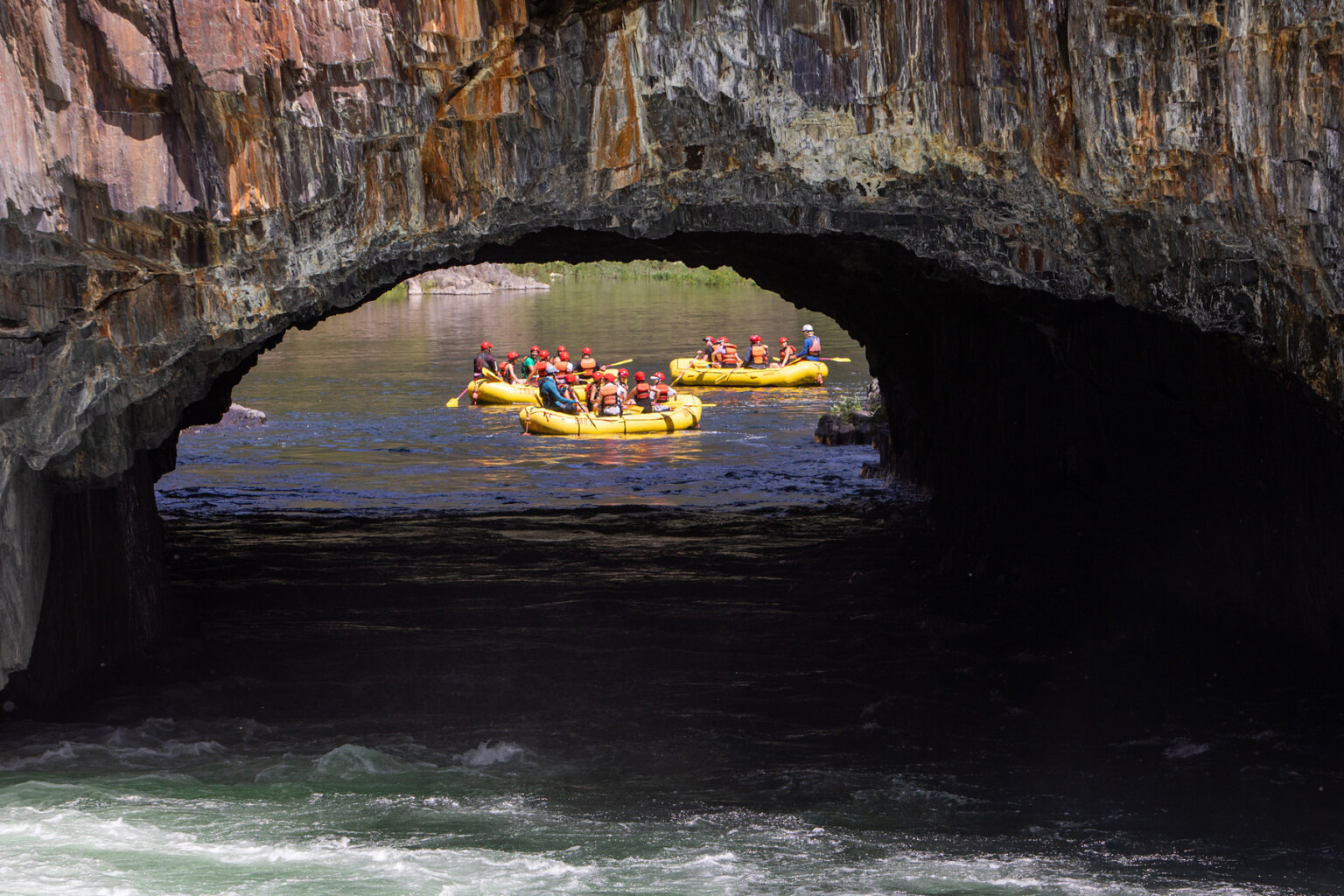 View through Tunnel Chute of three yellow rafts full of paddlers after they floated through the cave.