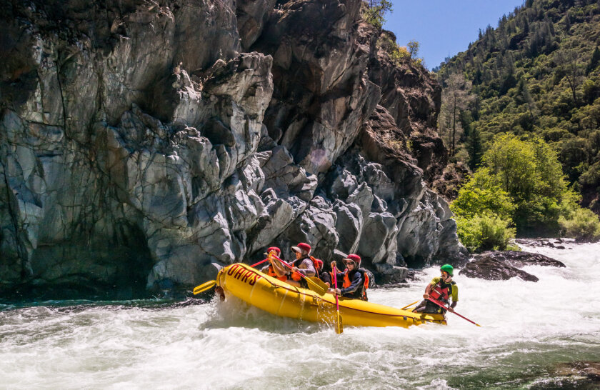 Side view of paddlers in a yellow raft with a guide in the back as they paddle through a stretch of whitewater on the Middle Fork American River.