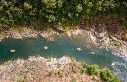 Aerial view of four yellow rafts as they make their way down the Middle Fork American River surrounded by rocky tree-studded shores.