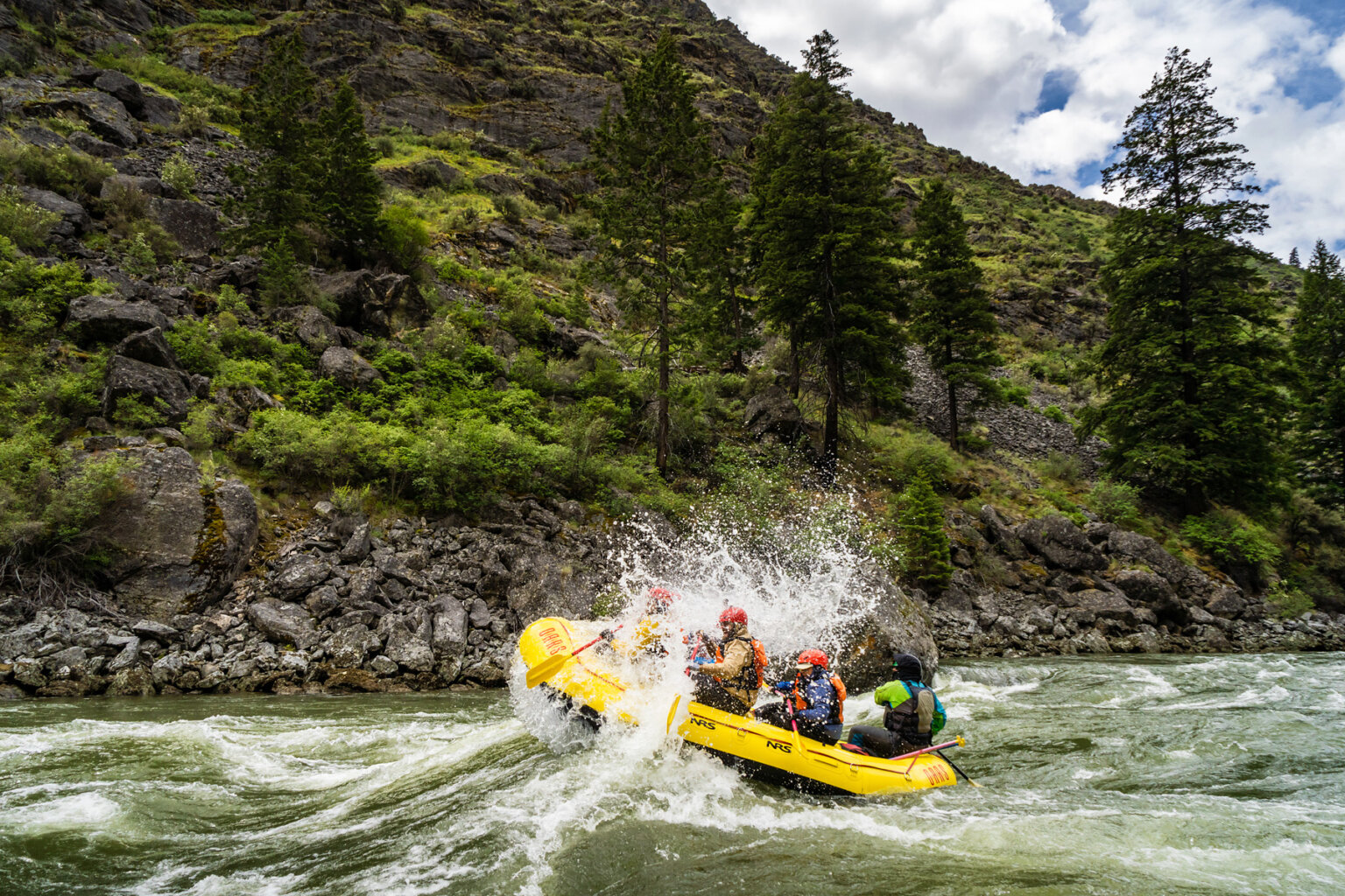 Side view of a boat full of paddlers as they crash through a wave on the Middle Fork of the Salmon River in Idaho.