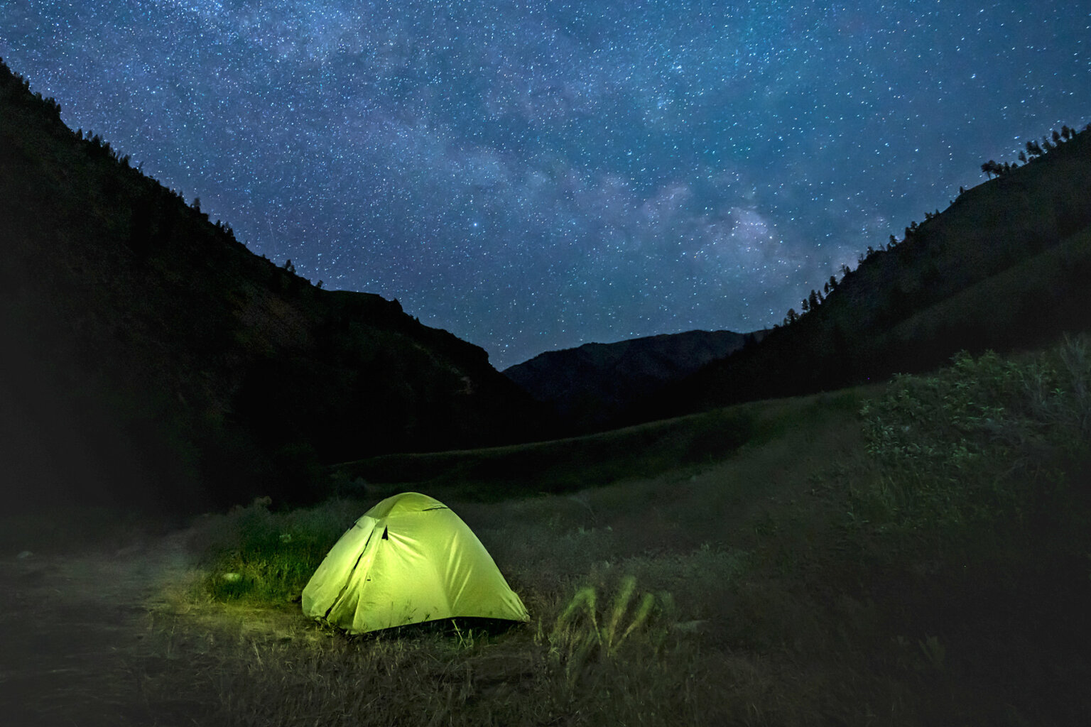 Night shot of a tent lit from inside and a vibrant star-studded sky.