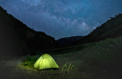 Night shot of a tent lit from inside and a vibrant star-studded sky.