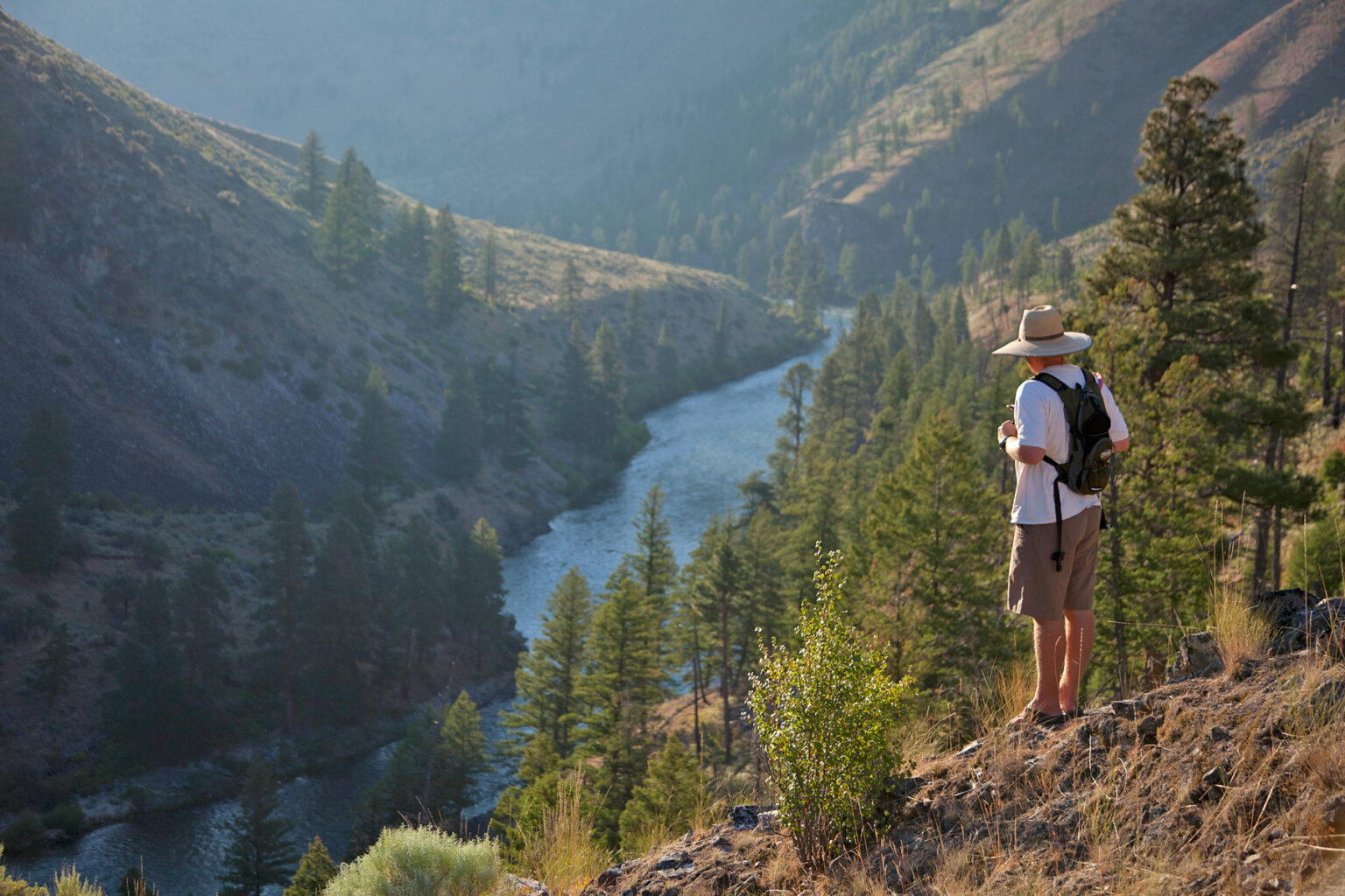 A hiker stands high above the Salmon River and takes in the view from a vista during an OARS rafting trip.