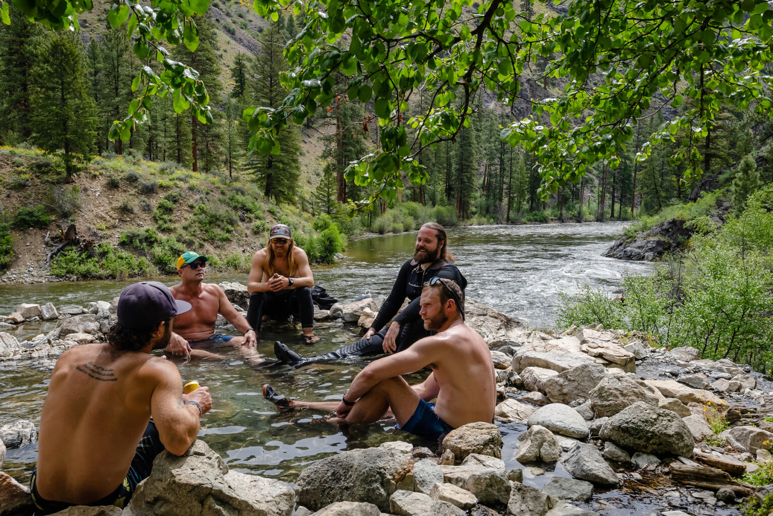 Five men sit in a small hots spring next to the river along the banks of the Middle Fork Salmon in Idaho.