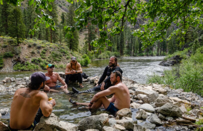 Five men sit in a small hots spring next to the river along the banks of the Middle Fork Salmon in Idaho.