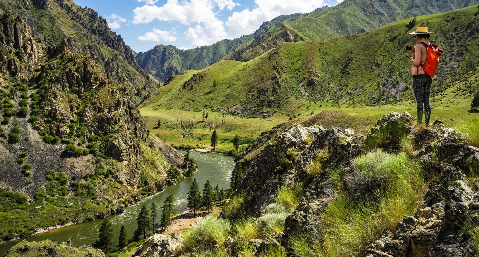 A woman stands atop a rocky cliff, admiring the scenic view of Idaho's Middle Fork of the Salmon River flowing beneath her.