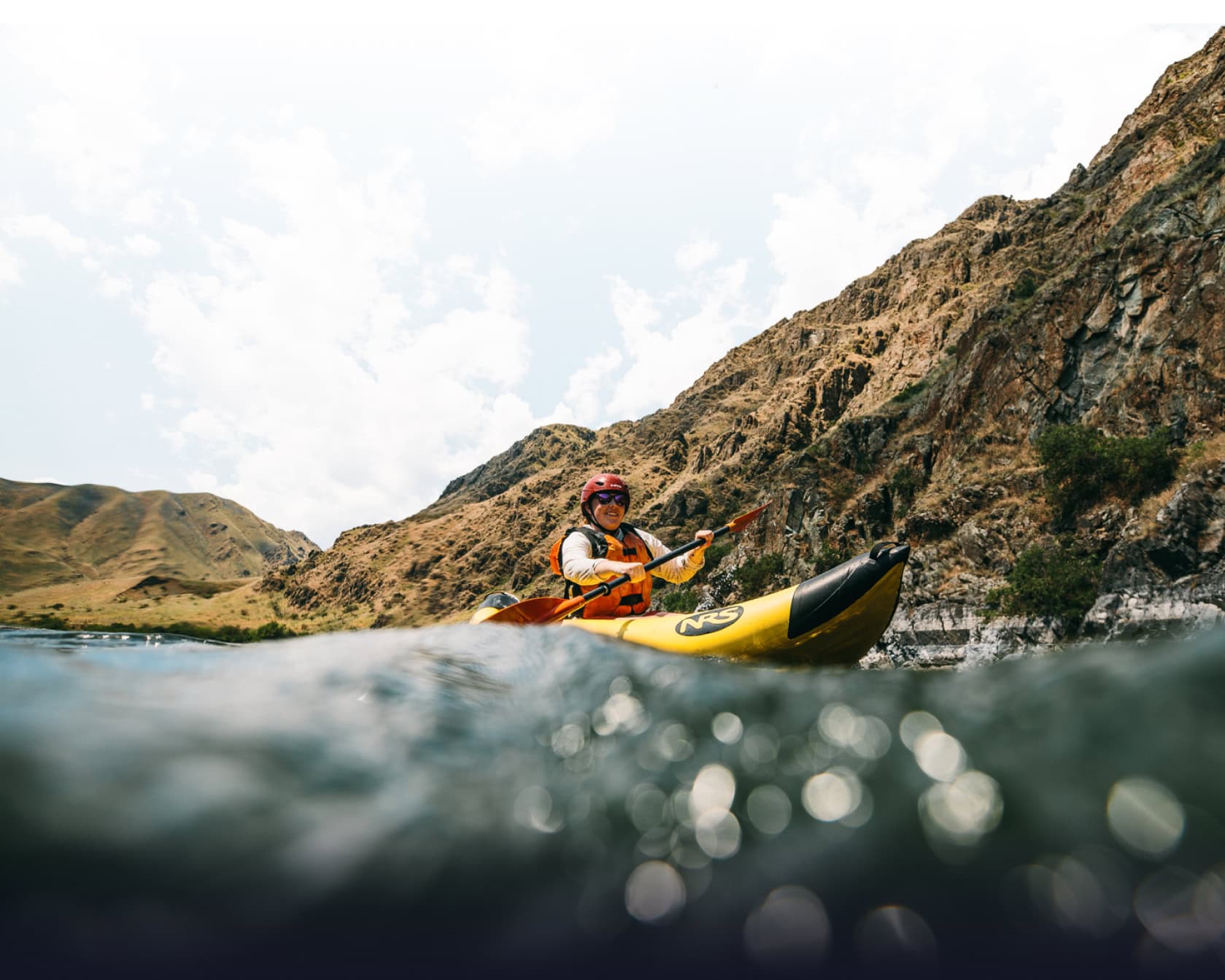 A woman in a yellow inflatable kayak paddles on the river.
